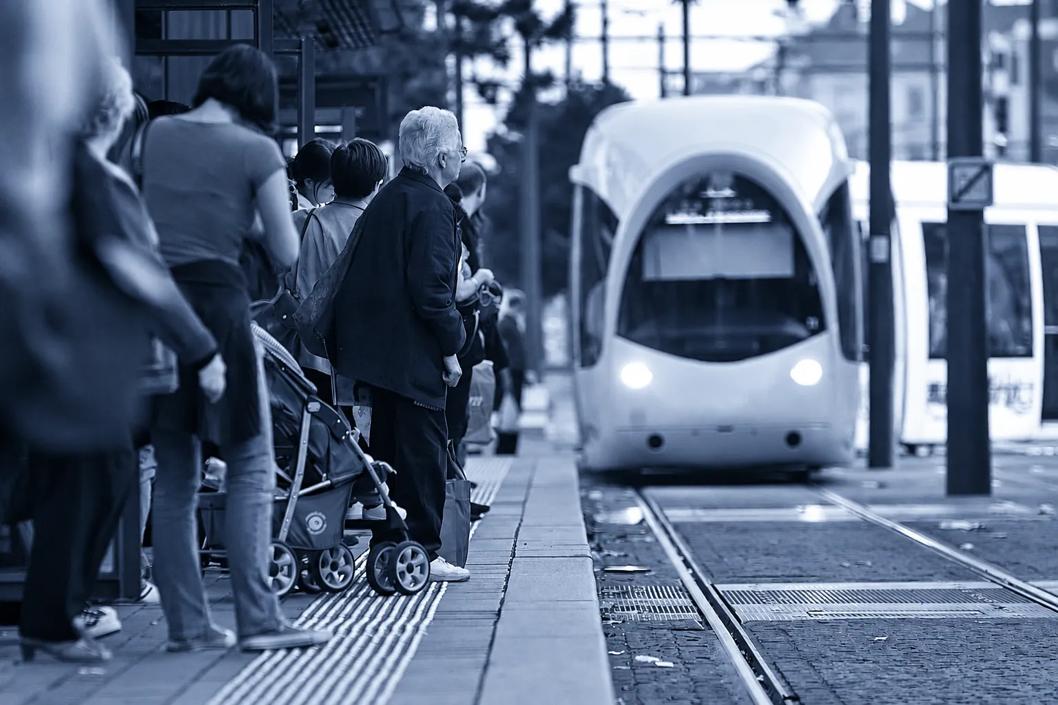 Tramvay durağında bekleyen, bebek arabalı ve yaşlı yolcuların da olduğu kalabalık